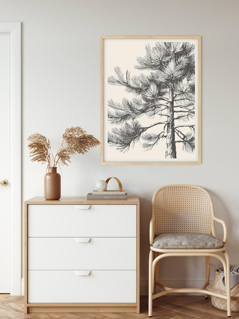 May include: A black and white illustration of a pine tree on a cream background. The illustration is framed in a light wood frame and hung on a white wall.