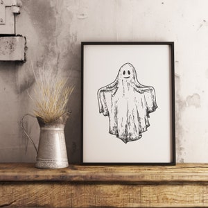 May include: A black and white illustration of a ghost with a smiling face in a black frame. The frame is on a wooden surface.