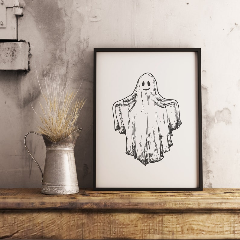 May include: A black and white illustration of a ghost with a smiling face in a black frame. The frame is on a wooden surface.