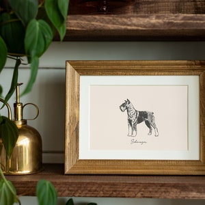 May include: A rectangular wooden frame containing a print of a black and white Schnauzer dog illustration on a light beige background. The word Schnauzer is printed in a cursive script font directly below the dog illustration within the frame.