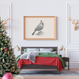 Puede incluir: Una impresi&oacute;n de arte mural horizontal enmarcada que presenta un boceto detallado en blanco y negro de un p&aacute;jaro cardenal posado en una rama, exhibida en un marco de madera clara sobre una cama con ropa de cama roja y verde y una manta de piel sint&eacute;tica.