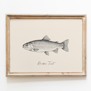Op de afbeelding: Een ingelijste print met een zwart-wit illustratie van een regenboogforel. De vis is in profiel afgebeeld op een cr&egrave;mekleurige achtergrond, met de woorden "Rainbow Trout" in een scriptlettertype. De lijst is lichtbruin van kleur.