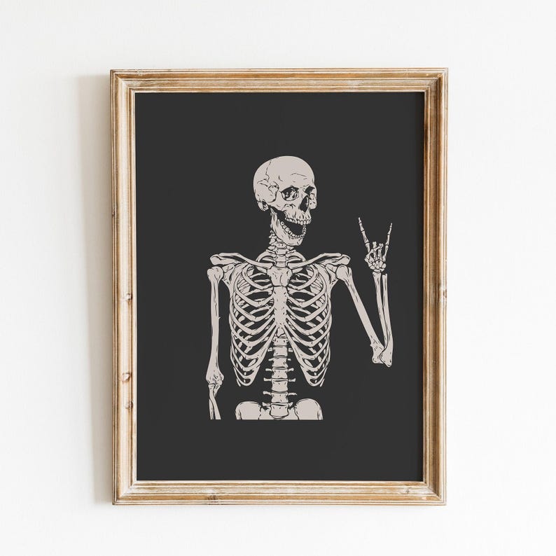 May include: A framed wall art print featuring a light beige skeleton illustration against a solid dark charcoal background. The skeleton is depicted from the chest up, with its mouth open and one hand raised in a rock and roll hand gesture.