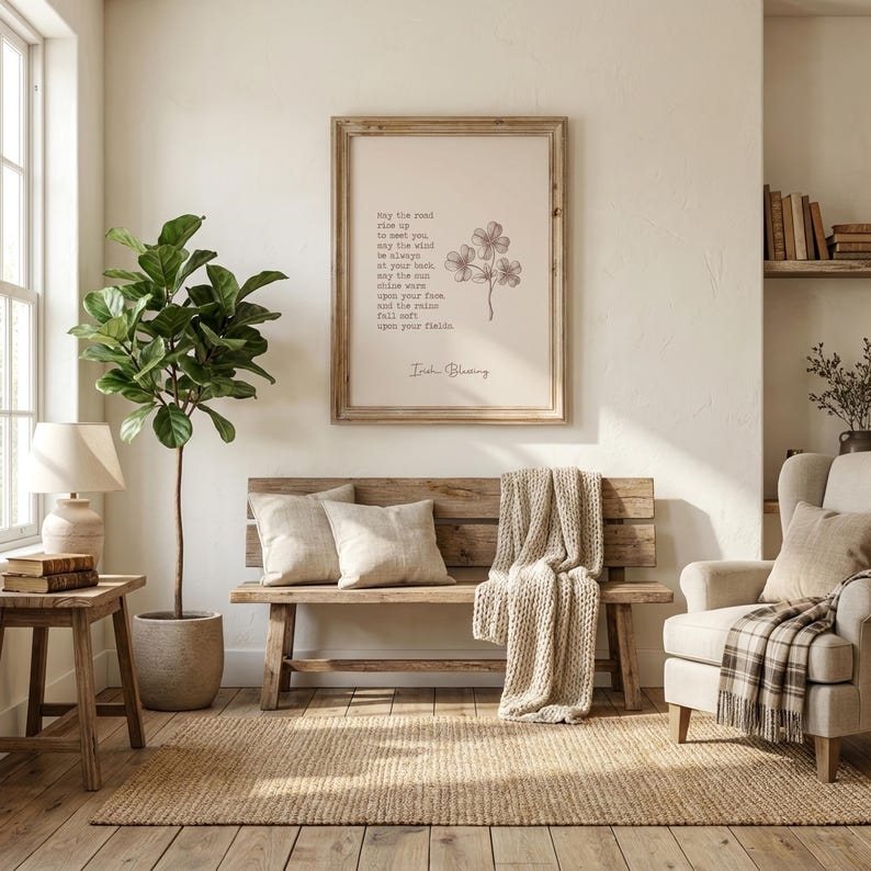 May include: A cozy living room scene with a wooden bench, pillows, and a woven throw. A framed print with text and a floral illustration hangs on the wall. A large potted plant and a side table with a lamp add to the warm ambiance.