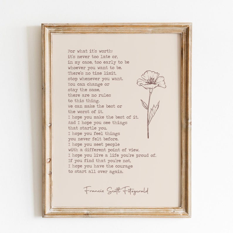 May include: A framed wall art print on a light beige background featuring the text of a quote by F. Scott Fitzgerald in a typewriter-style font, accompanied by a simple line drawing of a single flower on the right side, all in a wooden frame.