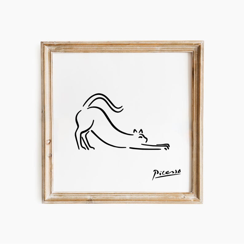 May include: A framed print with a minimalist black line drawing of a stretching cat. The artwork is signed "Picasso" in the lower right corner. The frame is light brown, and the background is white.