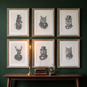 May include: Six framed animal portraits, each depicting a different animal in formal wear. Animals include a horse, owl, fox, deer, bear, and cat. The frames are light brown, and the background is a dark green. A candle and books are on a wooden table.