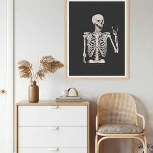 May include: A framed wall art print featuring a detailed illustration of a human skeleton against a dark charcoal background. The skeleton is depicted from the chest up, with its left hand raised in a rock-and-roll hand gesture and its mouth open.