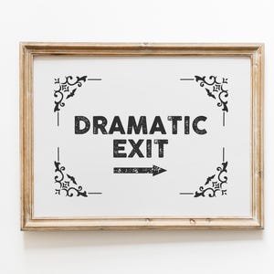 Op de afbeelding: Een ingelijst bord met de woorden "DRAMATIC EXIT" in een vet, verweerd lettertype. Het bord heeft decoratieve hoekaccenten en een pijl die naar rechts wijst, allemaal in zwart op een witte achtergrond. De lijst is lichtbruin.