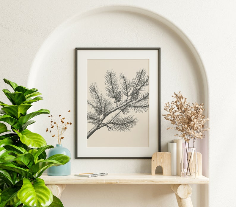 May include: A framed wall art print featuring a black and white line drawing of a pine branch with three pinecones on a solid beige background. The artwork is enclosed in a thin black rectangular frame, presenting a botanical illustration style.