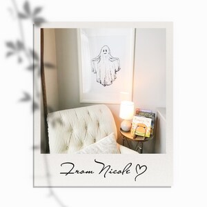 May include: A white armchair with a white and gray striped upholstery sits in a room with a framed black and white drawing of a ghost on the wall. A small table with a lamp and a stack of children's books sits next to the chair. The text "From Nicole" is written on the bottom of the image.