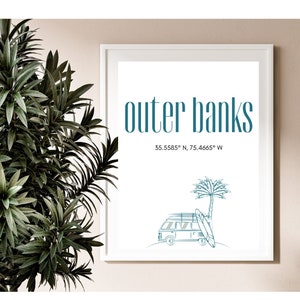 Puede incluir: Una impresión enmarcada en blanco con el texto "outer banks" en letras azul turquesa. Debajo del texto se encuentra la frase "35.5585° N, 75.4665° W" en una fuente más pequeña. La impresión presenta un dibujo lineal de una camioneta vintage con tablas de surf en el techo, estacionada debajo de una palmera.