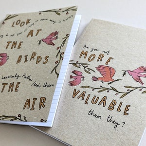 May include: Two small, brown notebooks with lined pages. The front cover of each notebook features a hand-drawn illustration of birds and branches. The text on the first notebook reads "Look at the birds heavenly Father feeds them the air". The text on the second notebook reads "Are you not more valuable than they?"