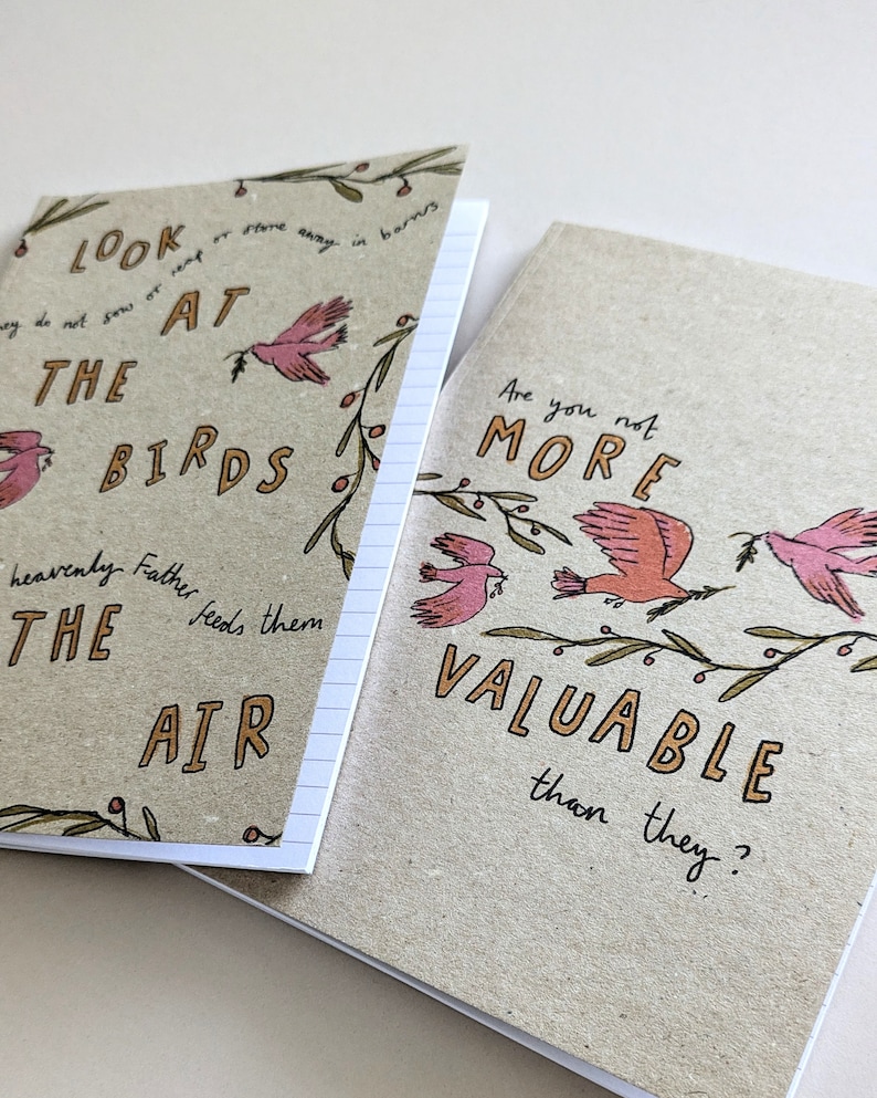 May include: Two small, brown notebooks with lined pages. The front cover of each notebook features a hand-drawn illustration of birds and branches. The text on the first notebook reads "Look at the birds heavenly Father feeds them the air". The text on the second notebook reads "Are you not more valuable than they?"