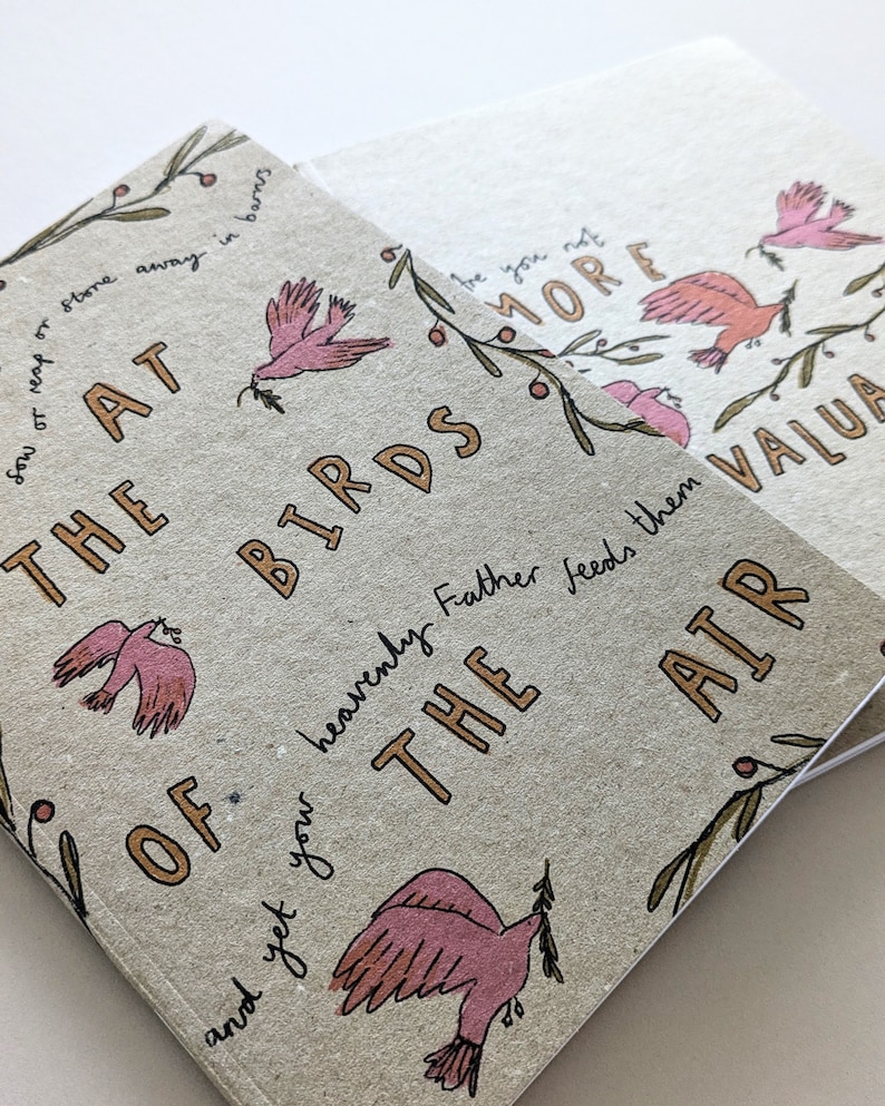 May include: A brown paper notebook with the text "The Birds of the Air" in gold lettering. The notebook features a pink bird illustration and a leafy branch with red berries.