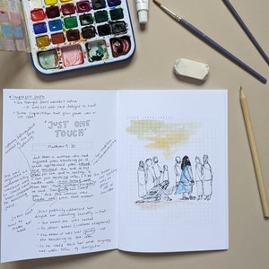 May include: An open notebook with a hand-drawn illustration of people in a line, with a woman in the centre reaching out to touch a man kneeling on the ground. The notebook page has handwritten text about the Bible verse Matthew 9:20, "Just One Touch." The page is gridded and has a watercolour wash in the top right corner.