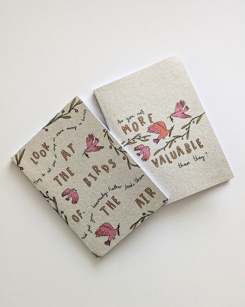 May include: Two small, brown, paper notebooks with a bird and floral design. The text on the notebooks reads "Look at the birds of...heavenly Father feeds them the air" and "Are you not more valuable than they?"