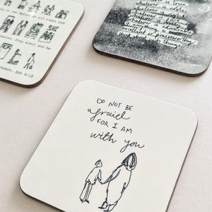 Può includere: Tre sottobicchieri quadrati con citazioni e illustrazioni ispiranti. Il primo sottobicchiere presenta un'illustrazione in bianco e nero di persone che pregano. Il secondo sottobicchiere presenta un'illustrazione in bianco e nero di una persona che tende la mano a un'altra persona. Il terzo sottobicchiere presenta un'illustrazione in bianco e nero di una persona con una citazione che dice "Non temere, perché io sono con te".