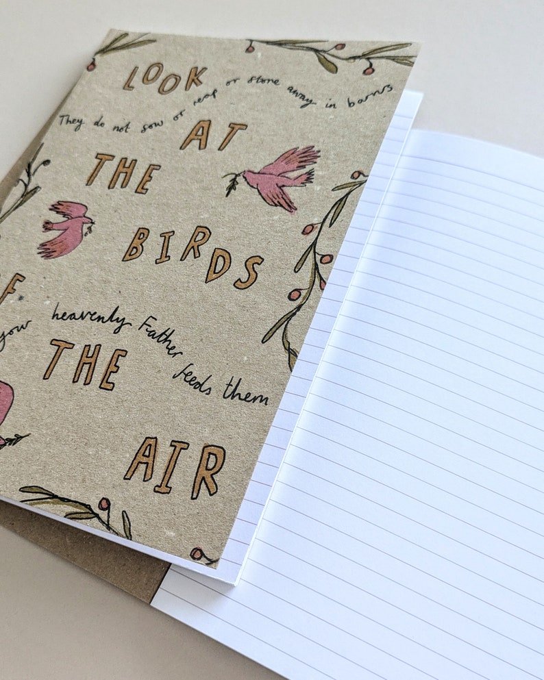 May include: A brown notebook with a quote about birds and a floral design. The quote reads "Look at the birds, they do not sow or reap or store away in barns, your heavenly Father feeds them, the air."