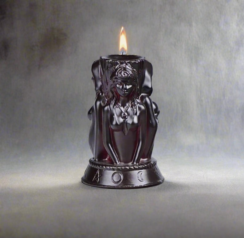 May include: Black candle with a detailed sculpted design of a woman with a crown and a necklace. The candle is lit and has a base with the symbols of the moon, sun, and a pentagram.