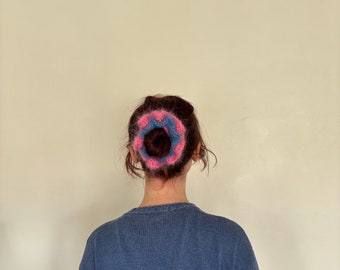 May include: A person with brown hair wearing a blue sweater with a pink and blue knitted hair scrunchie.