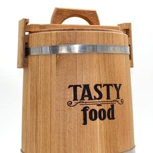 Può includere: Una botte di legno con una fascia metallica e un manico. La botte è etichettata "Tasty food".