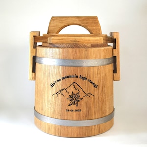 May include: A wooden barrel with a metal band and a handle. It has an engraved design with the text "Ain't no mountain high enough" and a date.