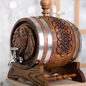 Puede incluir: Un barril de madera con un diseño de águila tallada y un grifo de metal. El barril está sobre un soporte de madera con un asa decorativa.