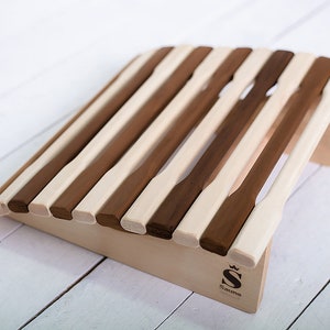 Può includere: Una panca per sauna in legno con forma curva e doghe di legno chiaro e scuro alternate. La panca ha una piccola base in legno con la parola "Sauna" e un logo a corona.