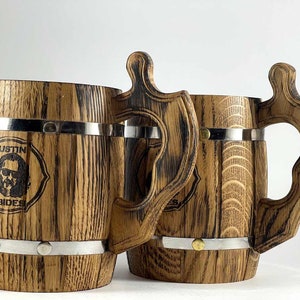 May include: Two wooden beer steins with metal bands and handles. The stein on the left has a personalized design with the text "Justin Abides".