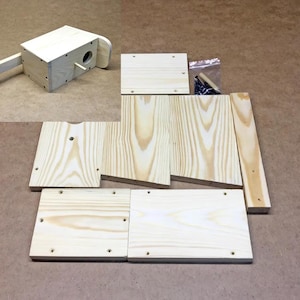 Könnte beinhalten: Ein Vogelhaus-Bausatz aus Holz mit vorgeschnittenen Teilen und einem teilweise montierten Vogelhaus. Das Set enthält verschiedene Holzplatten, einen kleinen Dübel und Schrauben. Das Holz hat eine natürliche, helle Farbe mit sichtbarer Maserung.