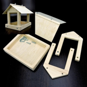 Op de afbeelding: Een houten vogelvoederkit, niet gemonteerd, met een schuin dak. De kit bevat de hoofdstructuur, het dak, de basis en hardware. De natuurlijke houtkleur is zichtbaar, met metalen schroeven voor de montage. De voederbak is ontworpen om op te hangen.