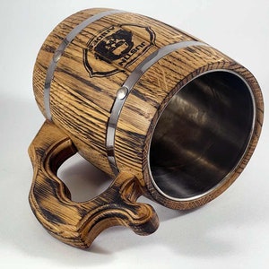 May include: A wooden beer stein with a stainless steel interior. The stein has a dark wood finish and is decorated with a metal band and a personalized inscription that reads "Justin's Lodge".