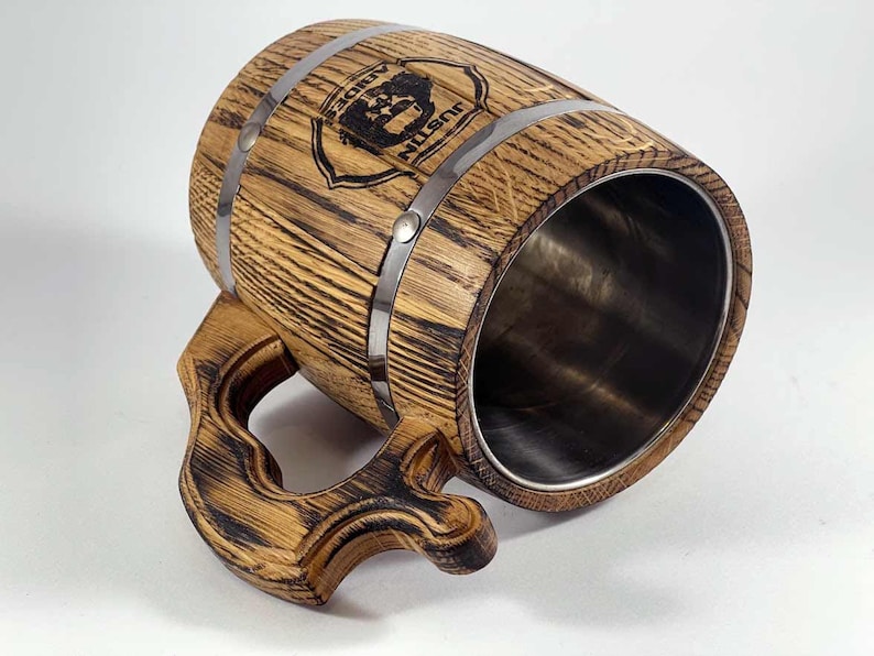 May include: A wooden beer stein with a stainless steel interior. The stein has a dark wood finish and is decorated with a metal band and a personalized inscription that reads "Justin's Lodge".