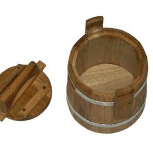 May include: A wooden bucket with a lid. The bucket is made of light brown wood and has two silver bands around it. The lid is also made of wood and has a handle.
