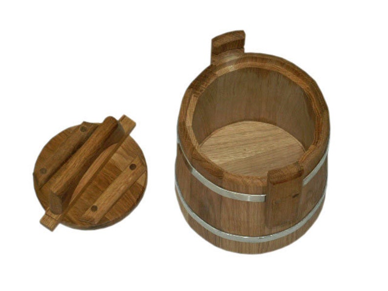 May include: A wooden bucket with a lid. The bucket is made of light brown wood and has two silver bands around it. The lid is also made of wood and has a handle.