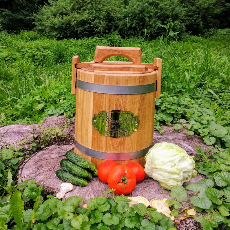 May include: A wooden barrel with a metal band and a brass plaque that reads "Homemade Pickles". The barrel is sitting on a tree stump with cucumbers, tomatoes, and a head of cabbage around it.