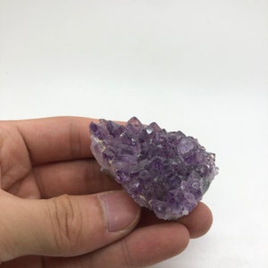 May include: A cluster of amethyst crystals in various shades of purple, with some crystals having a lighter, almost clear appearance. The crystals are arranged in a natural, irregular formation.