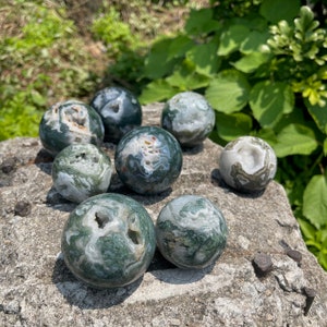 Puede incluir: Una colecci&oacute;n de ocho esferas de &aacute;gata verde y blanca, cada una con un patr&oacute;n &uacute;nico de colores y texturas en espiral. Las esferas est&aacute;n dispuestas sobre una superficie gris y texturizada.