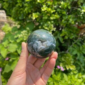 Puede incluir: Una esfera de &aacute;gata verde, blanca y rosa. La esfera es lisa y pulida, con un patr&oacute;n de remolino de verde, blanco y rosa.