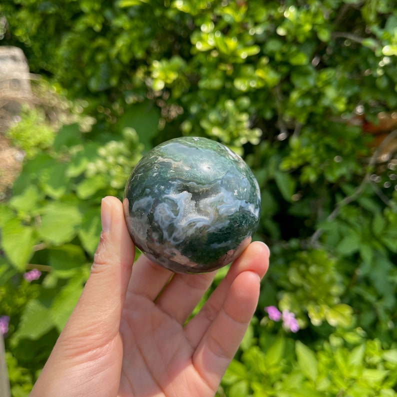 Puede incluir: Una esfera de &aacute;gata verde, blanca y rosa. La esfera es lisa y pulida, con un patr&oacute;n de remolino de verde, blanco y rosa.