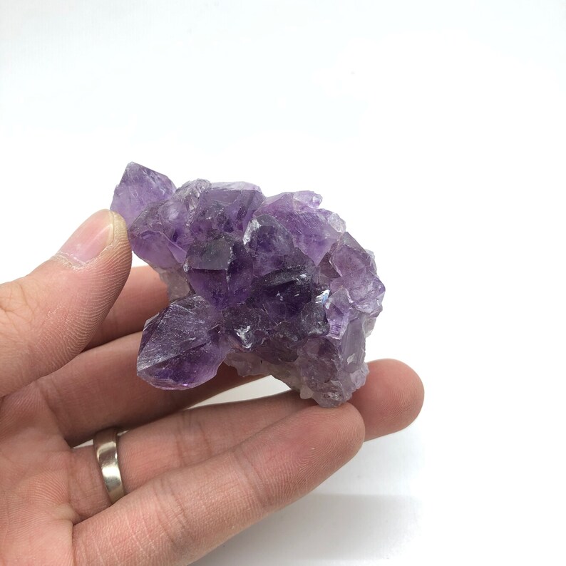 May include: A cluster of amethyst crystals in various shades of purple. The crystals are clustered together in a natural formation, creating a unique and beautiful piece.