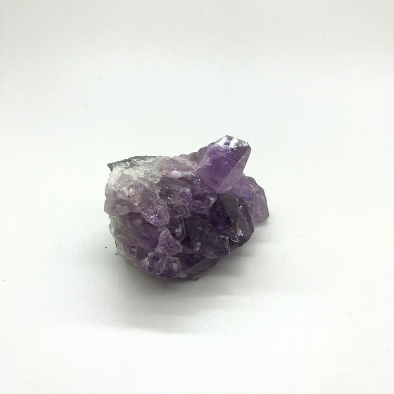 May include: A cluster of amethyst crystals in shades of purple and white. The crystals are arranged in a natural, organic shape.
