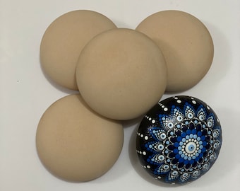 May include: Five round, smooth stones. Four are a solid beige color, and one is black with a blue and white mandala design. The mandala stone has a central eye symbol.