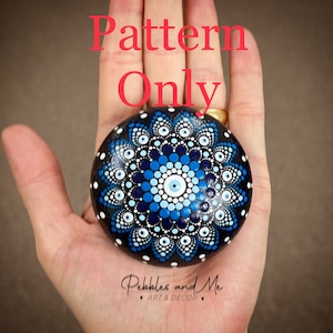 May include: A hand-painted rock with a blue and white mandala design. The mandala features a central eye design surrounded by concentric circles of blue, white, and black dots.