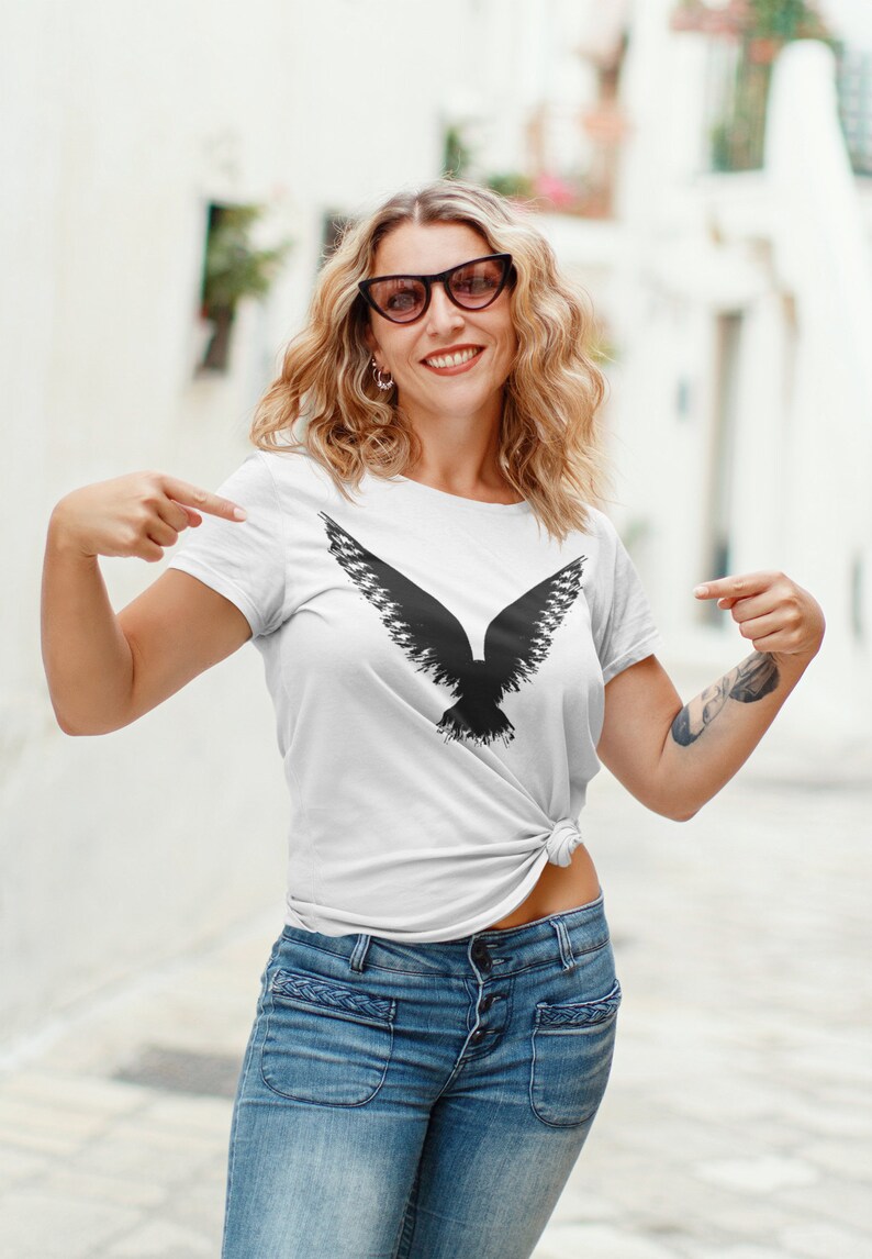 Gothic graphic shirt depicting a Raven design, worn by a witchy female model. Bella Canvas gothic tees are 100% Airlume combed & ringspun cotton made in the USA. Norse apparel with cotton fabric and Viking Raven graphic logo.