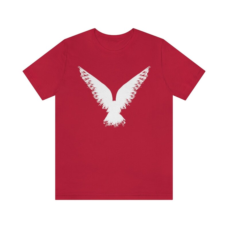 May include: Red short-sleeved t-shirt with a white stylized image of a bird with its wings spread.