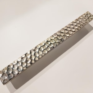 May include: A silver hammered metal cabinet pull with a textured surface.