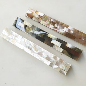 May include: Three decorative hair clips made of mother of pearl tiles. The clips are in different colours: white, brown, and pink.