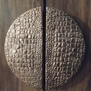 May include: A pair of round, half-circle door handles with a textured, crocodile-skin pattern. The handles are made of a gold-toned metal.
